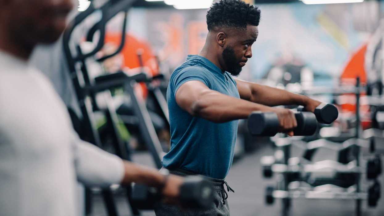 Focused athlete performing lateral raises with dumbbells, building shoulder muscles in a modern fitness center