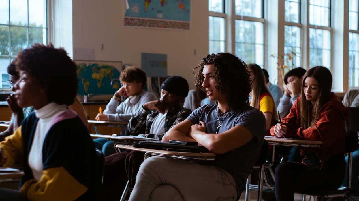 Group of young adult students sit at desks in classroom listening to teacher