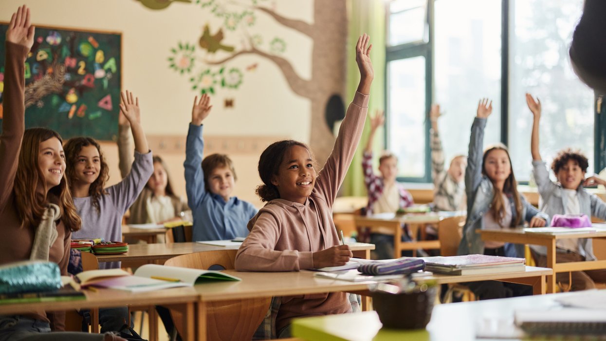 Happy elementary students raising their hands on a class at school
