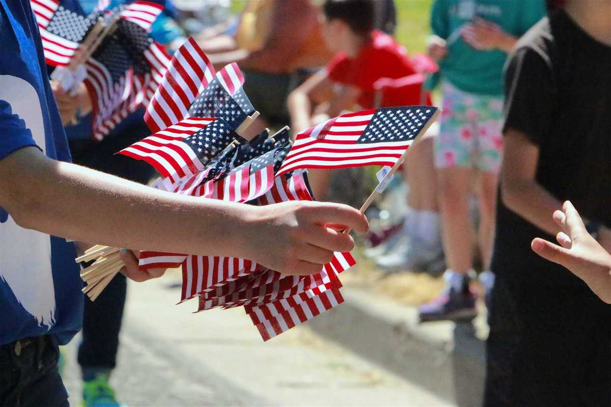 Human Hand Passing Out American Flags Parade Route Blurred Crowd in Background