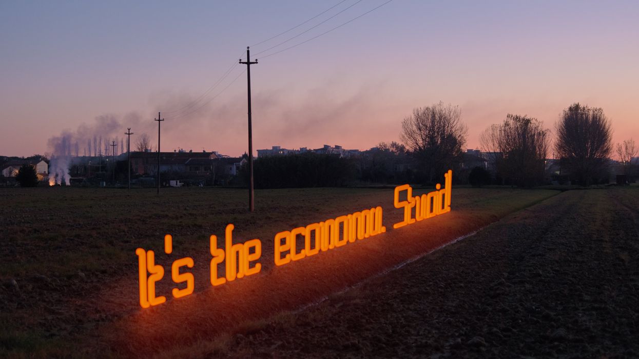 "It's the economy, stupid!"; is written with a neon light in the countryside at dusk