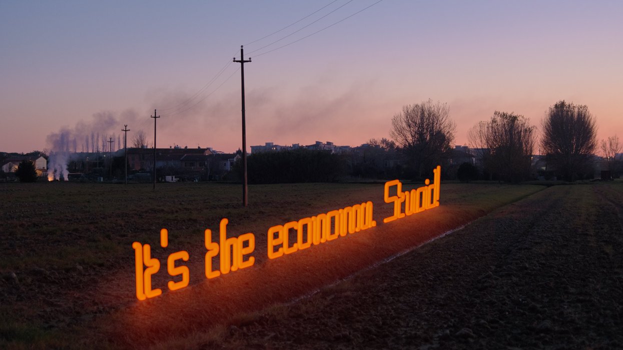 "It's the economy, stupid!"; is written with a neon light in the countryside at dusk
