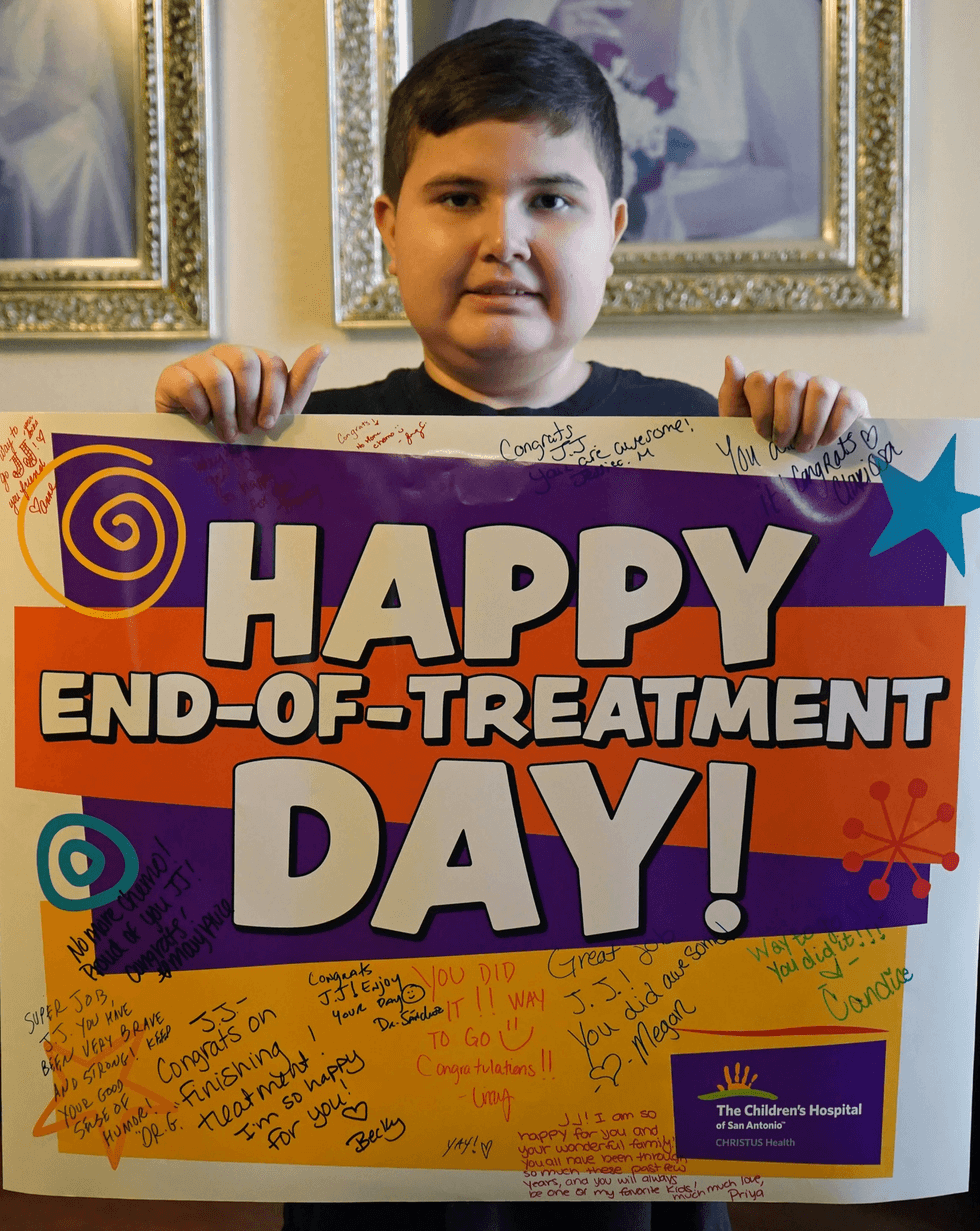 Juan Jose \u201cJ.J.\u201d Nevares holds his end-of-treatment day poster from The Children's Hospital of San Antonio at his home