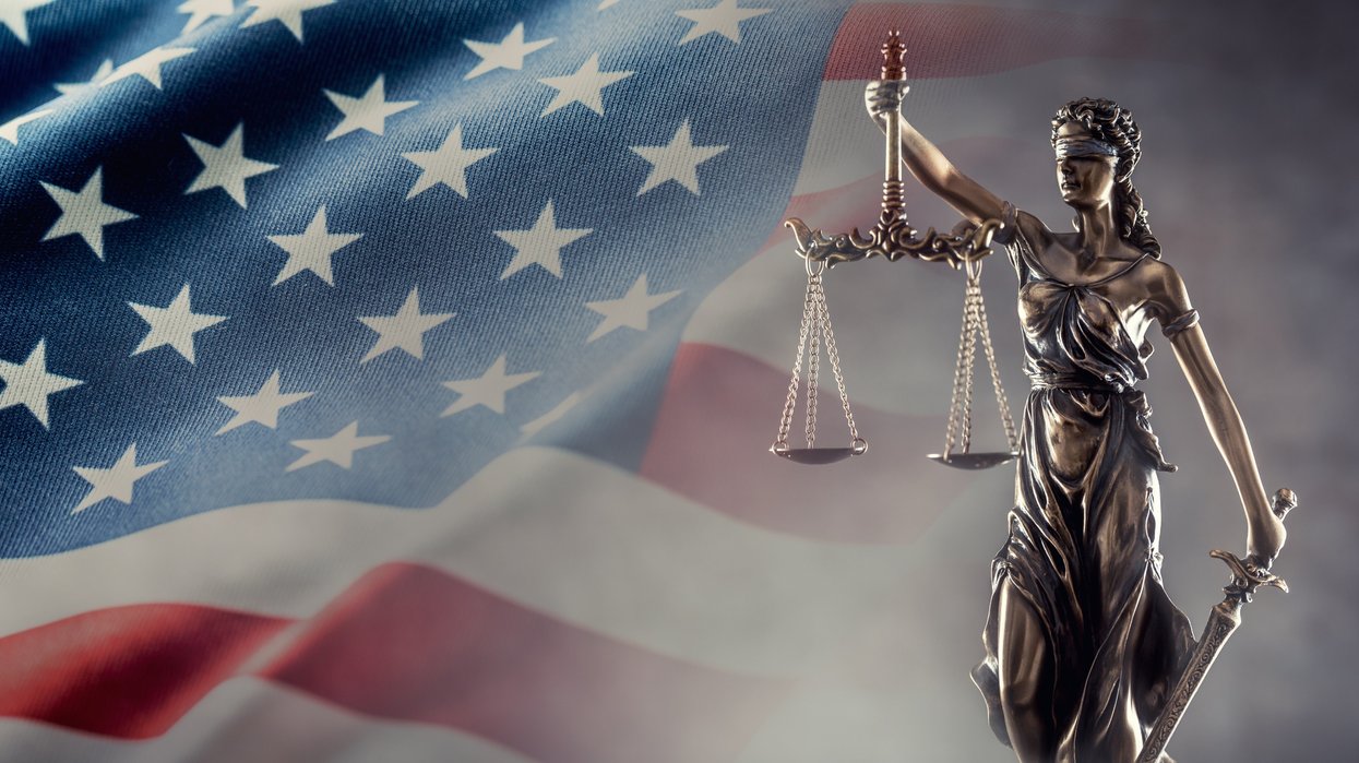 Justice is blind statue symbolizing law with scales and sword in hands and a US flag in the background