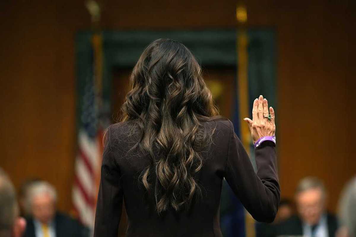 Kristi Noem facing away with her hand up to be sworn in as she testifies.