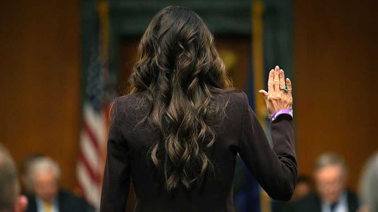 Kristi Noem facing away with her hand up to be sworn in as she testifies.