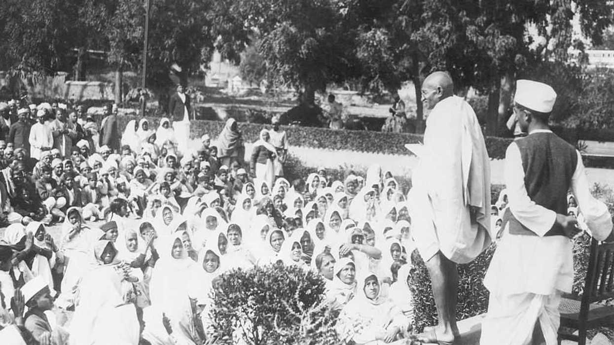 Mahatma Gandhi addressing some of his thousands of followers on a lawn.