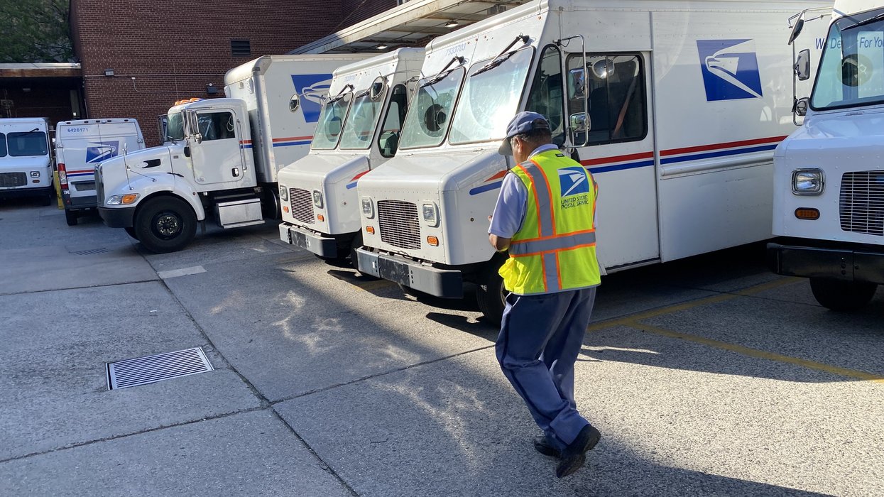 Mail delivery person in safety vest walking towards USPS delivery trucks