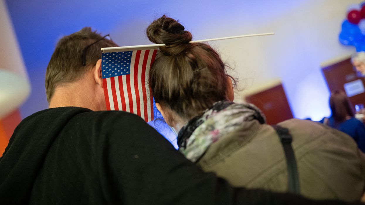 Man and woman standing close together. She has an American flag sticking out of her hair.