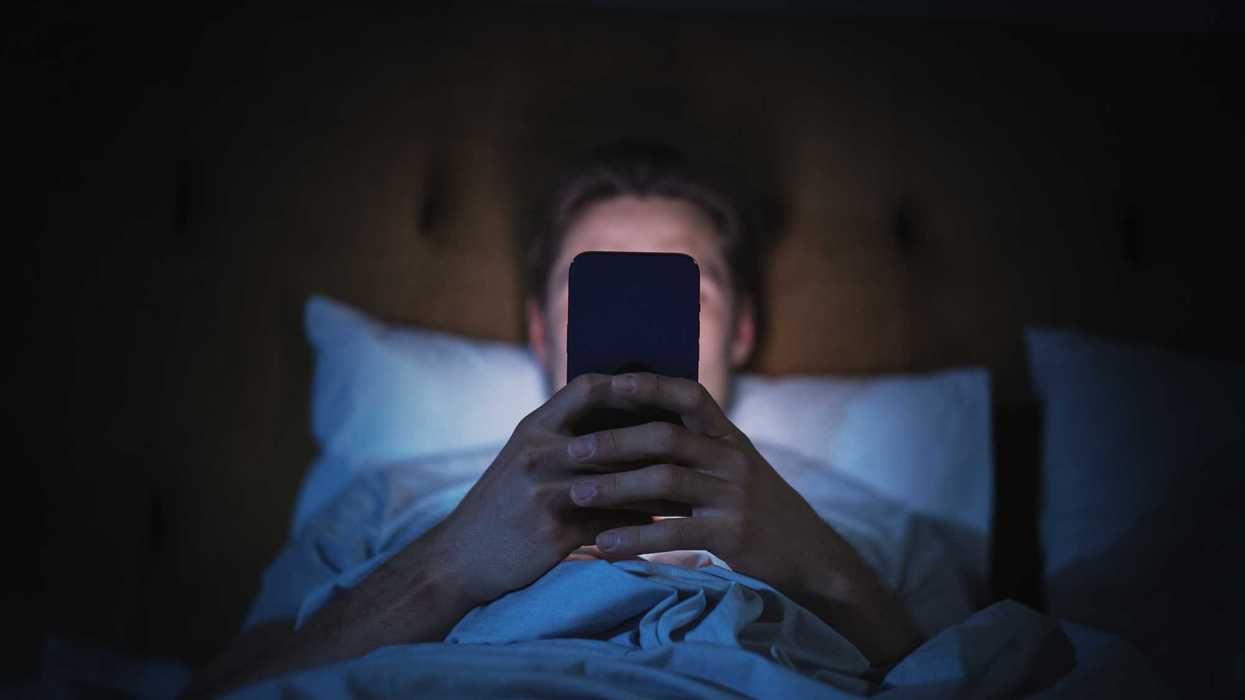 Man lying in his bed, on his phone at night.