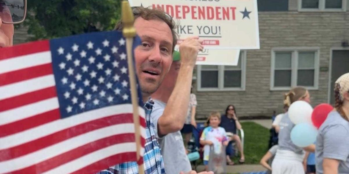 Michael Bridgford holding an American flag and an "Independent Like You" sign at an Iowa campaign event
