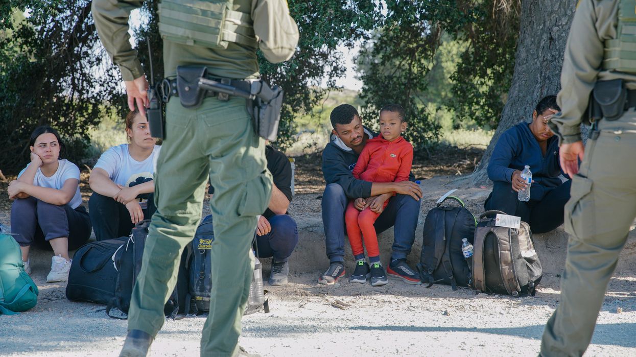 Migrants sits on the ground facing Border Patrol agents