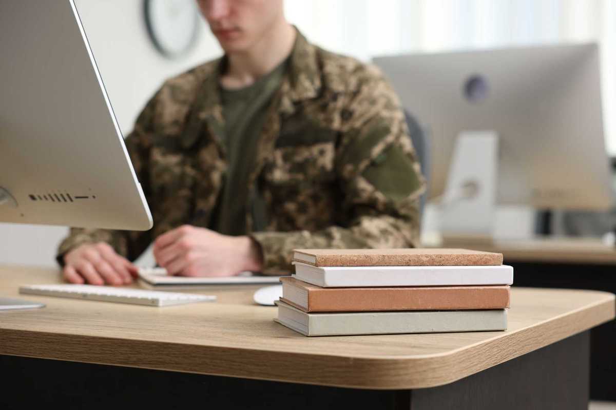 Military education. Student in soldier uniform learning at wooden table indoors, selective focus