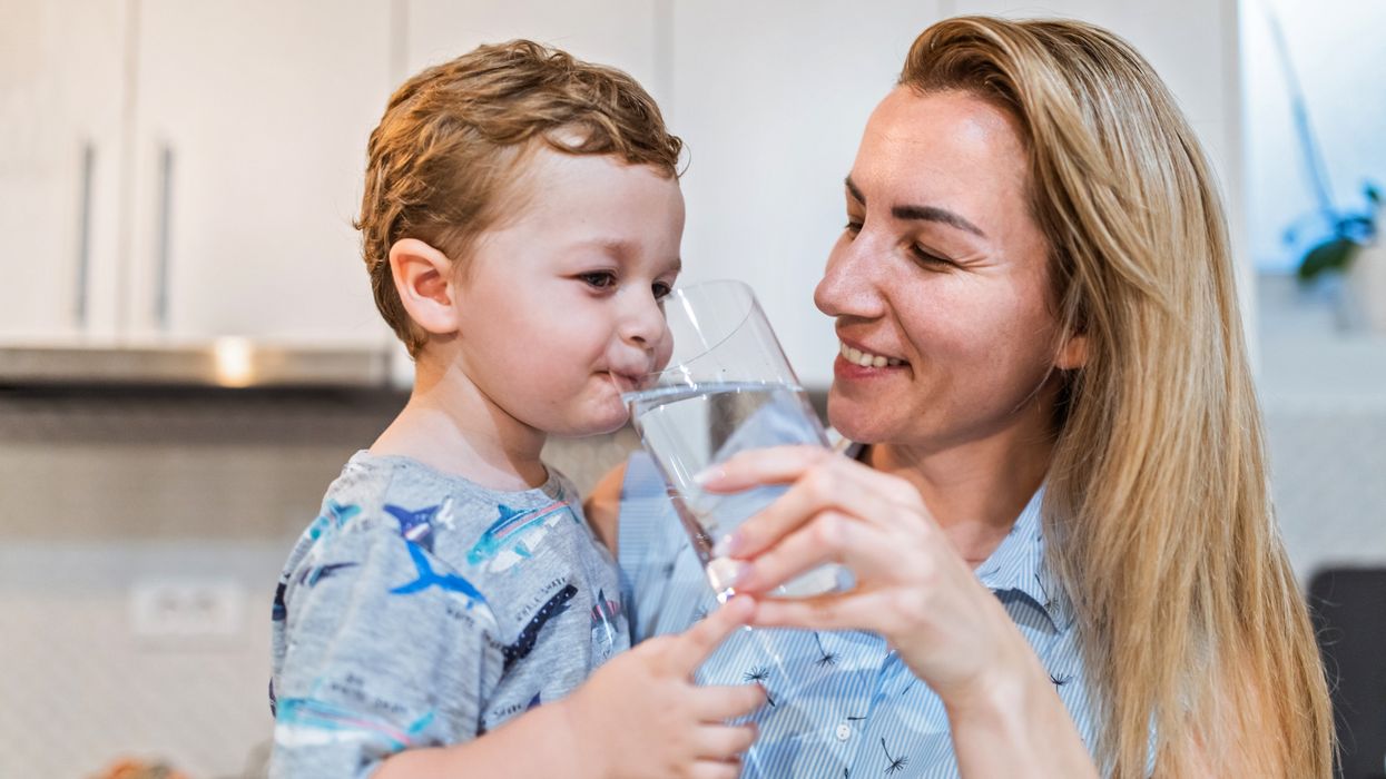 Mother offering a glass of water to her toddler son.