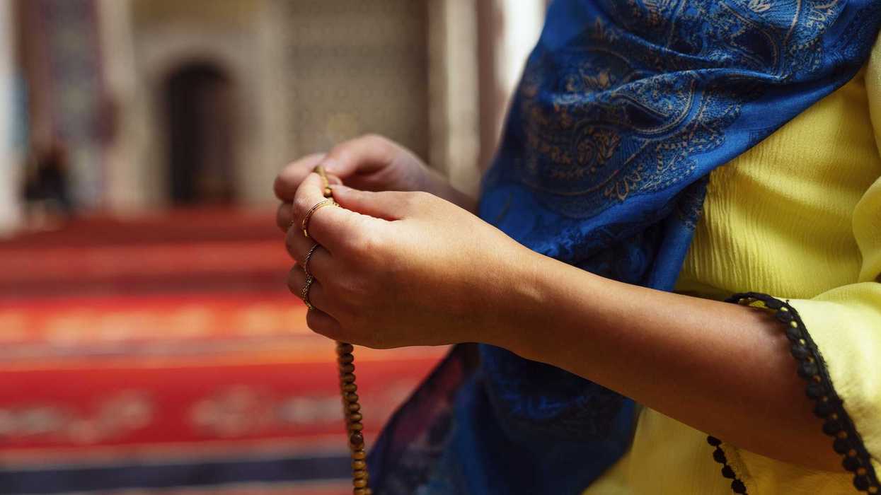 Muslim woman in headscarf and hijab prays with her hands up in air while holding prayer beads in mosque.Religion praying concept