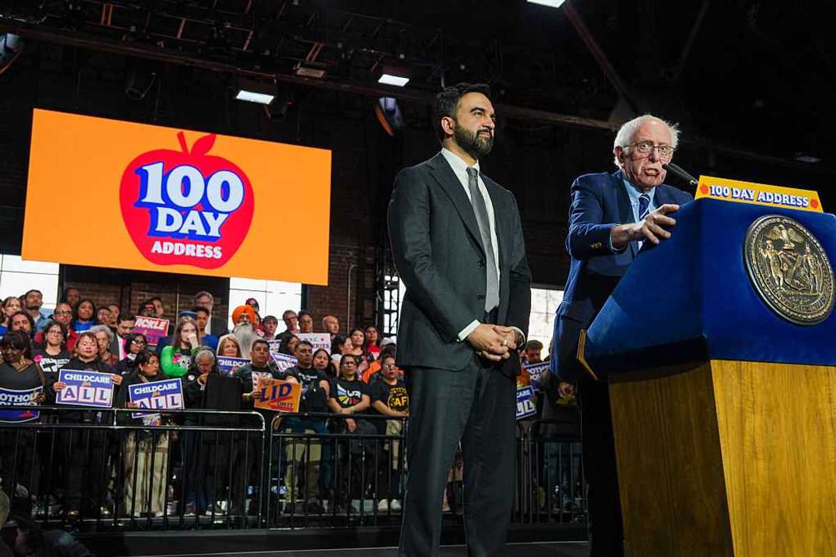 New York City Mayor Zohran Mamdani and US Senator Bernie Sanders standing at a podium together with a crowd of supporters behind them.