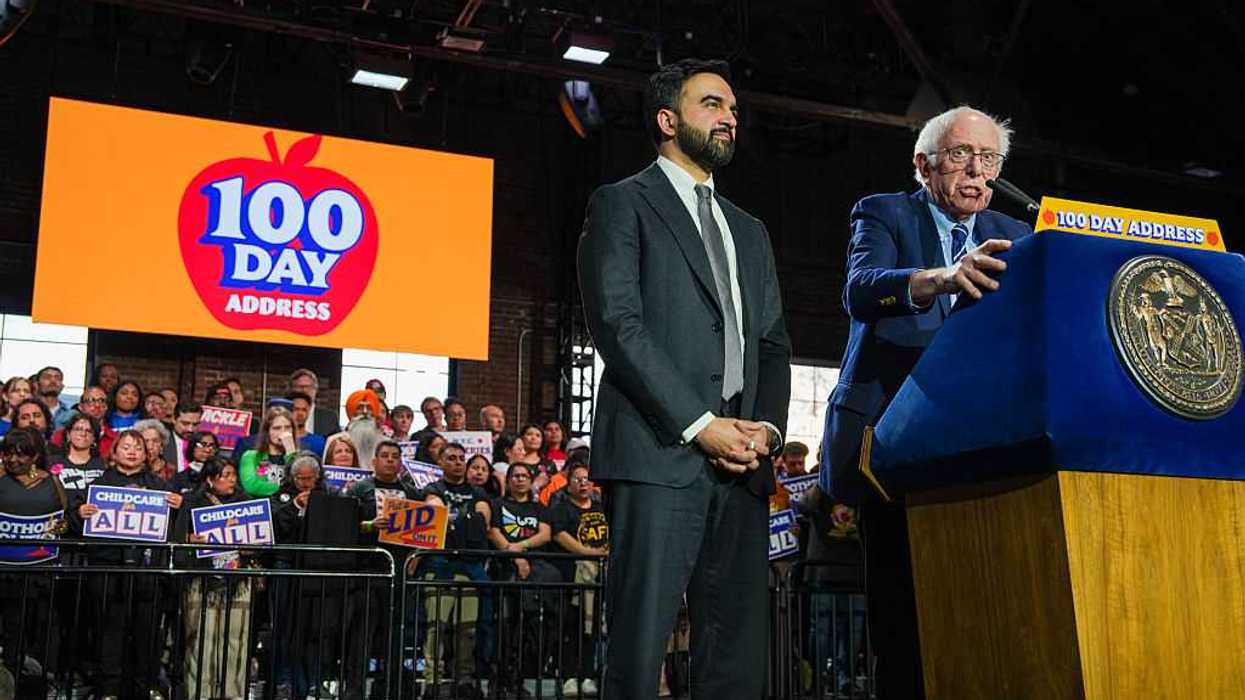 New York City Mayor Zohran Mamdani and US Senator Bernie Sanders standing at a podium together with a crowd of supporters behind them.