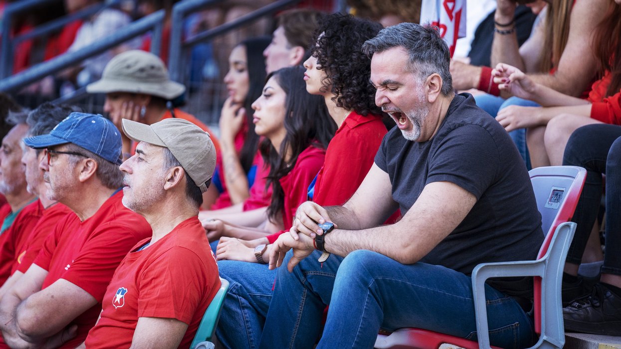 Older adult male in crowd of fans yawns and checks the time on his watch