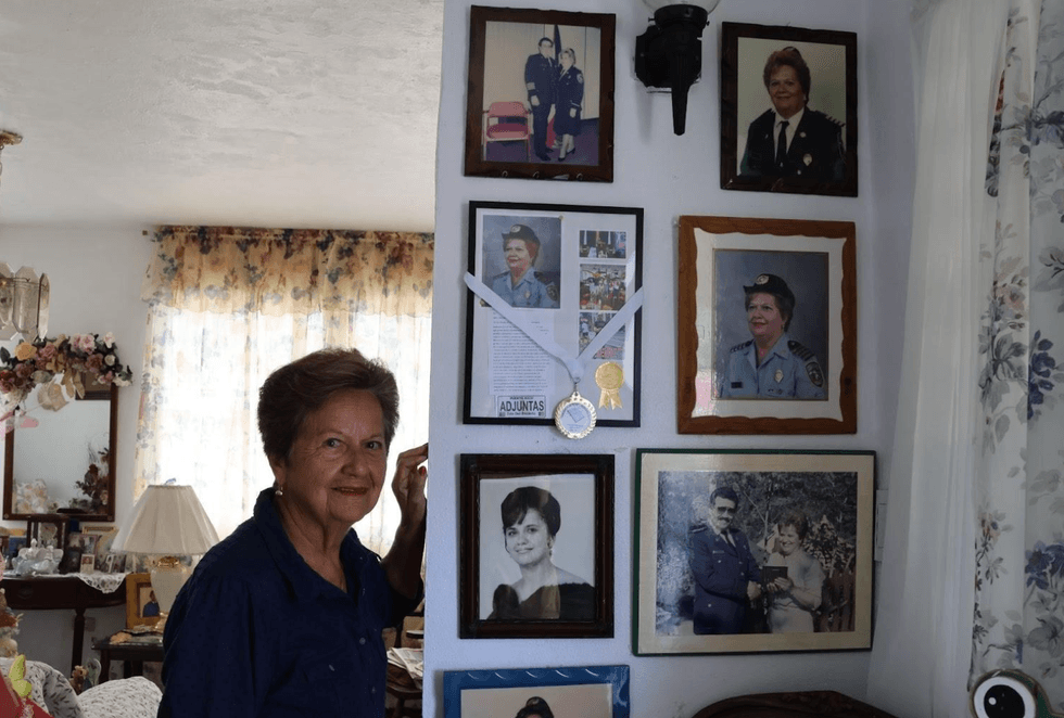 Olga Hern\u00e1ndez Molina stands with a wall of portraits in her home. She served on Adjuntas\u2019 community police force for many years.