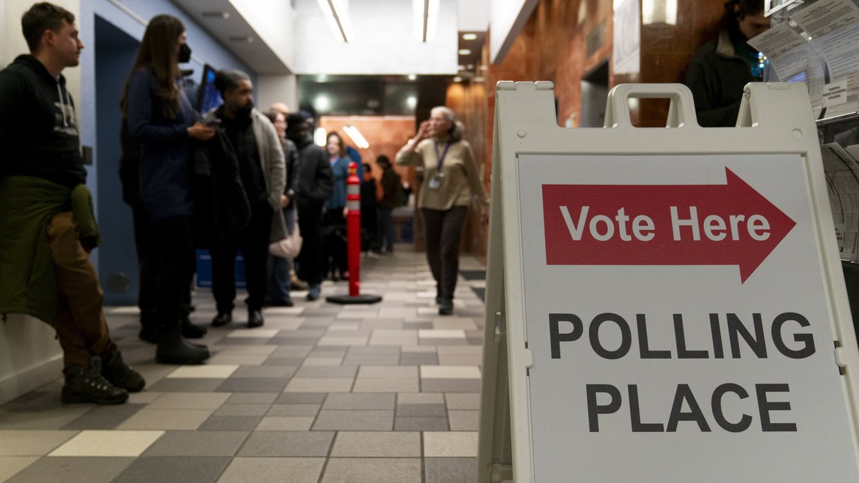 Peopel waiting in line near a sign that reads "Vote Here: Polling Place"