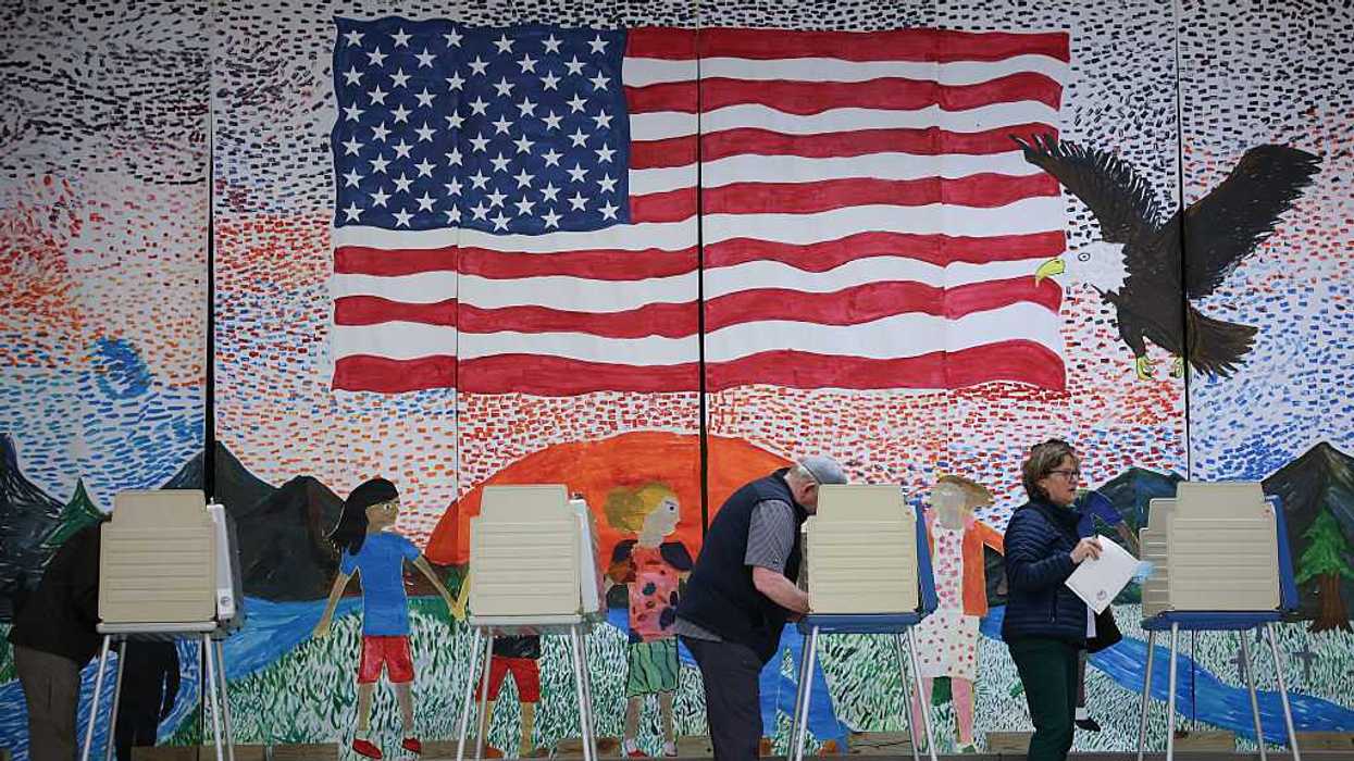 People at voting booths, casing their votes in front of a mural depicting the American flag, a bald eagle flying, and children holding hands in the foreground.