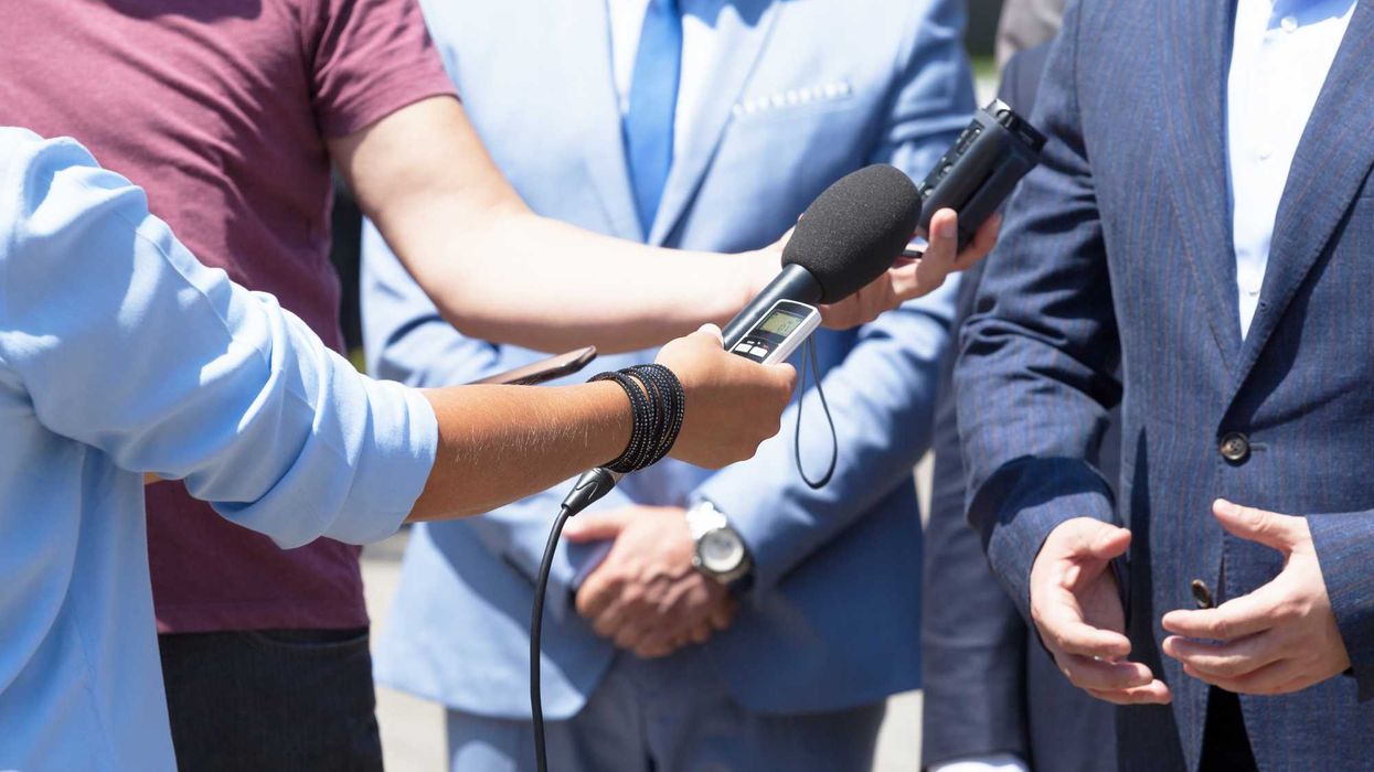 People holding microphones and recorders to someone who is speaking.