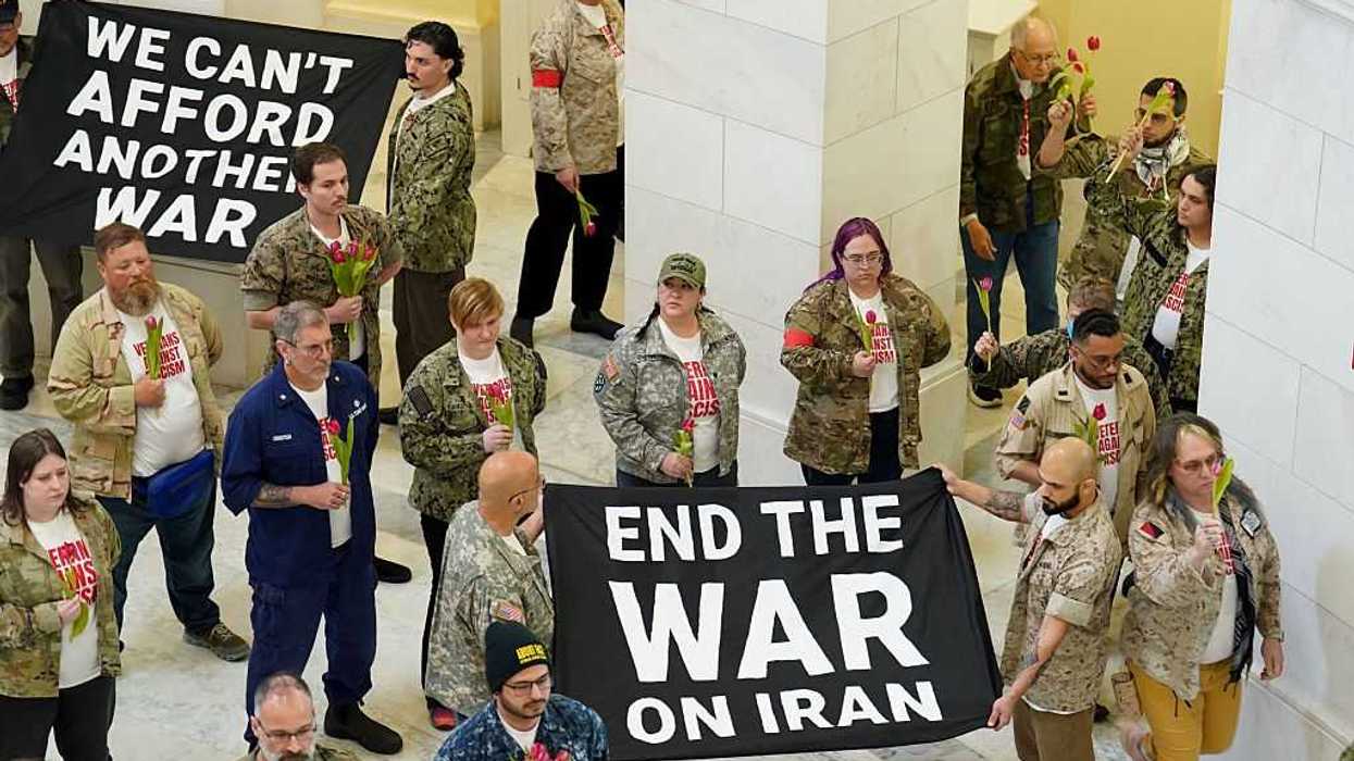 People protesting in the Cannon House Office Building on Capitol Hill, holding tulips and signs that read, "We can't afford another war" and "end the war on iran.'