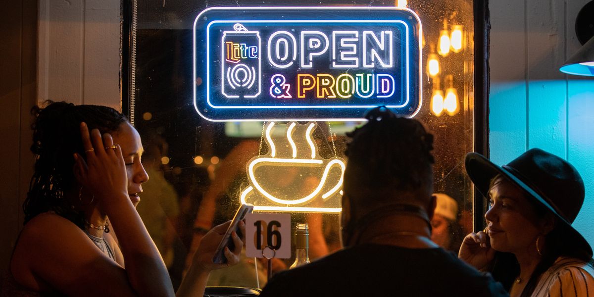 People sitting beneath a sign that reads, "Open & Proud"