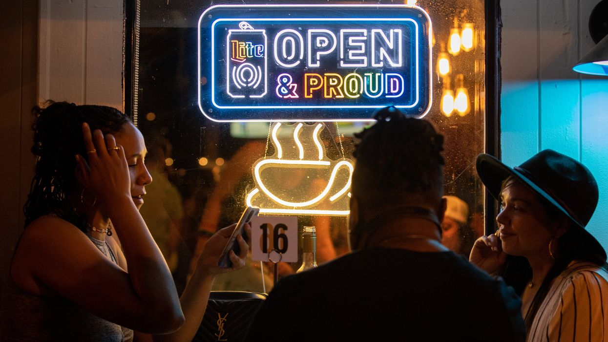People sitting beneath a sign that reads, "Open & Proud"
