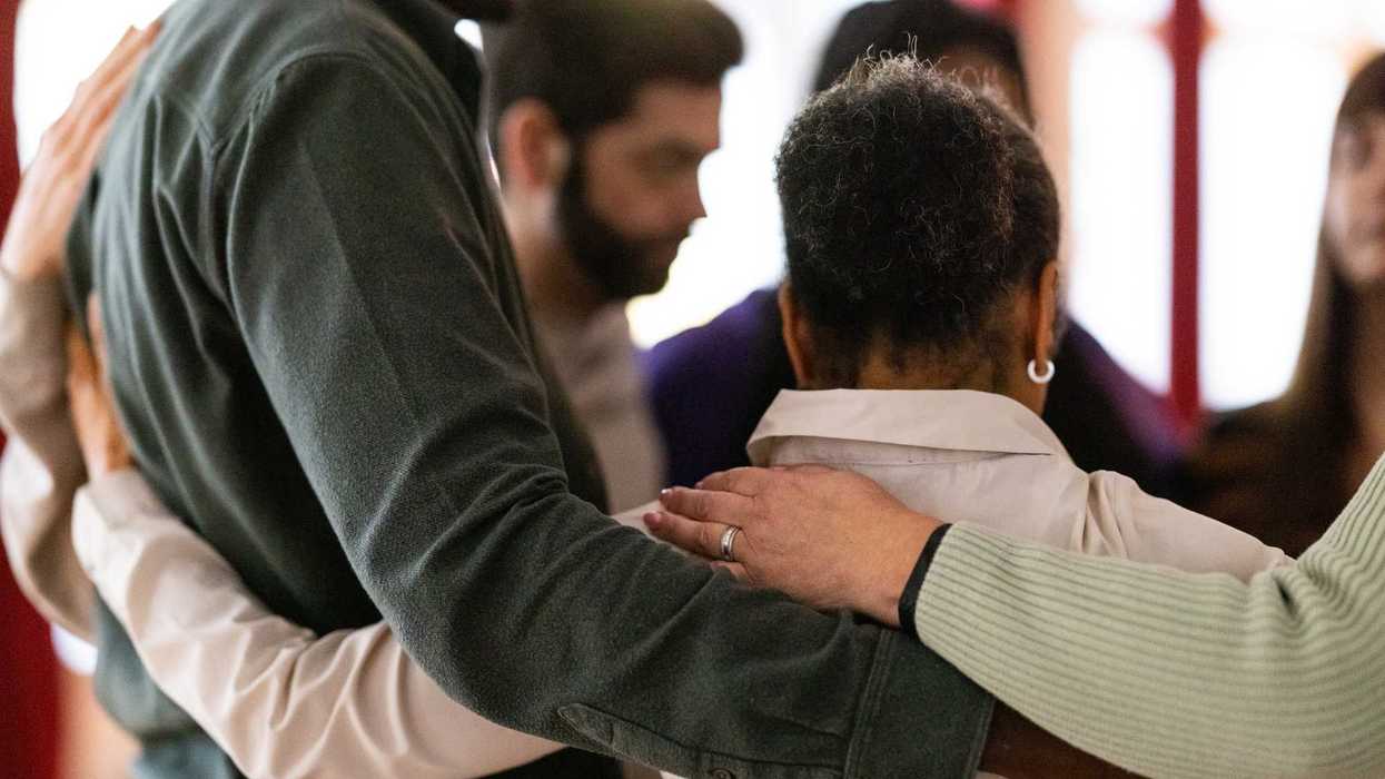 People standing in a circle with their arms around each other.
