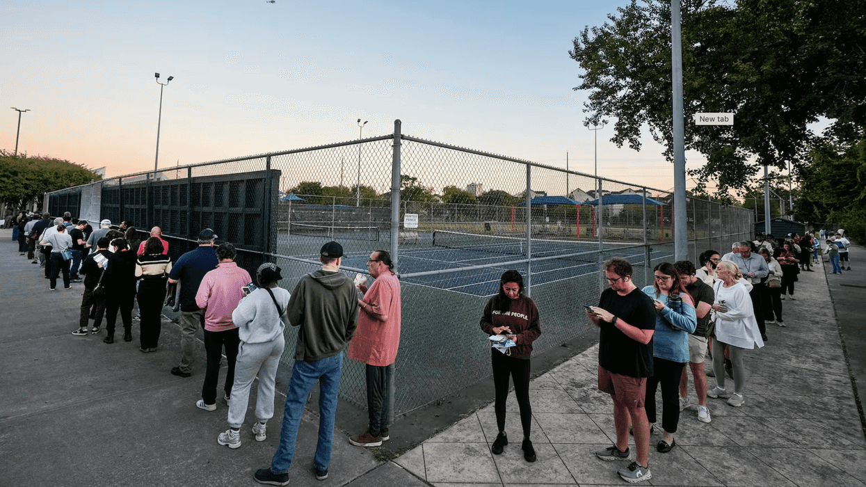People waiting in a line outside as the sun sets.
