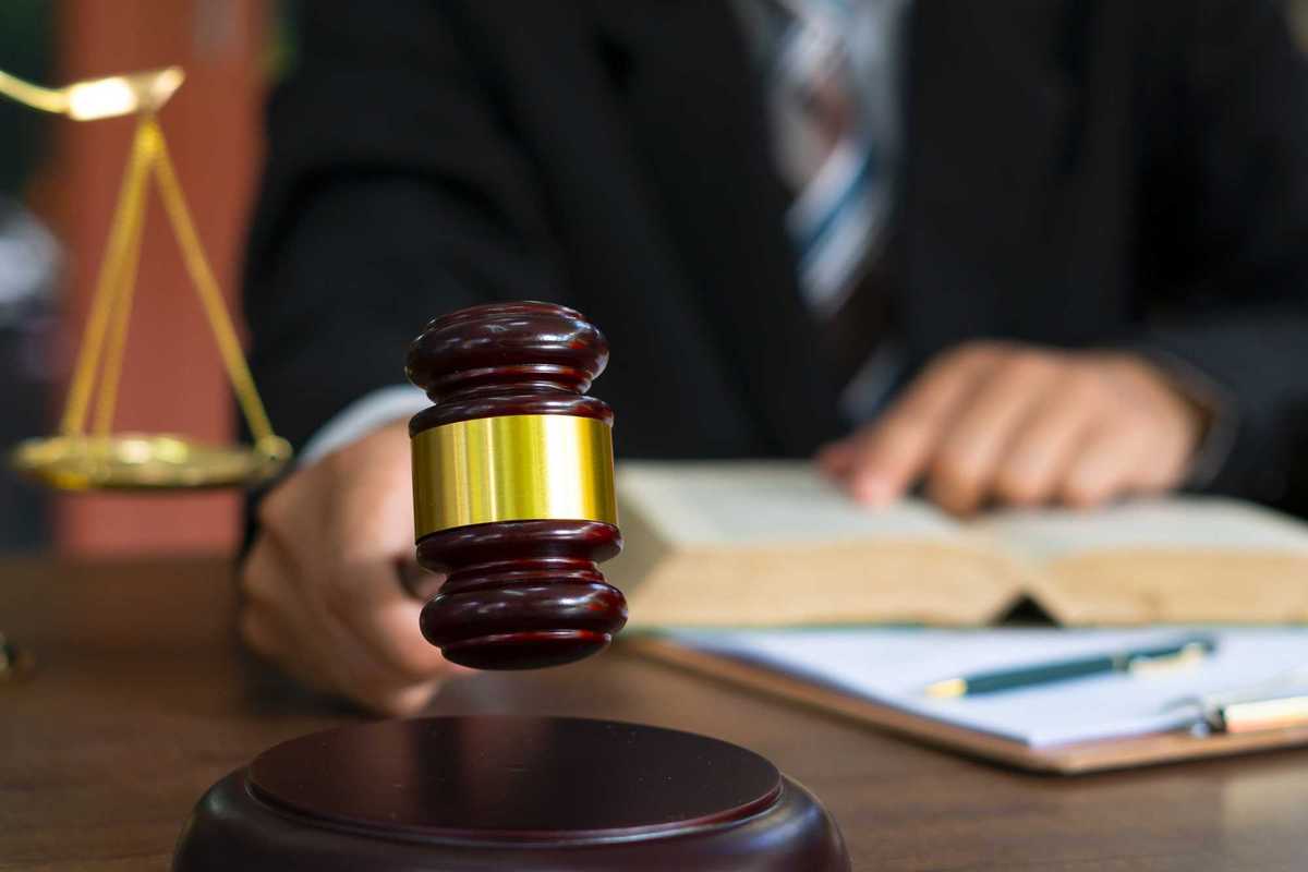 Person holding gavel and reading from a book.