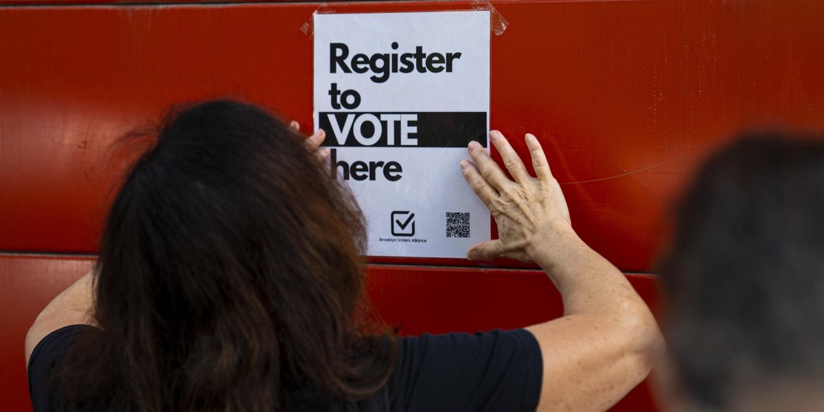 Person posting a sign that reads, "Register to vote here"