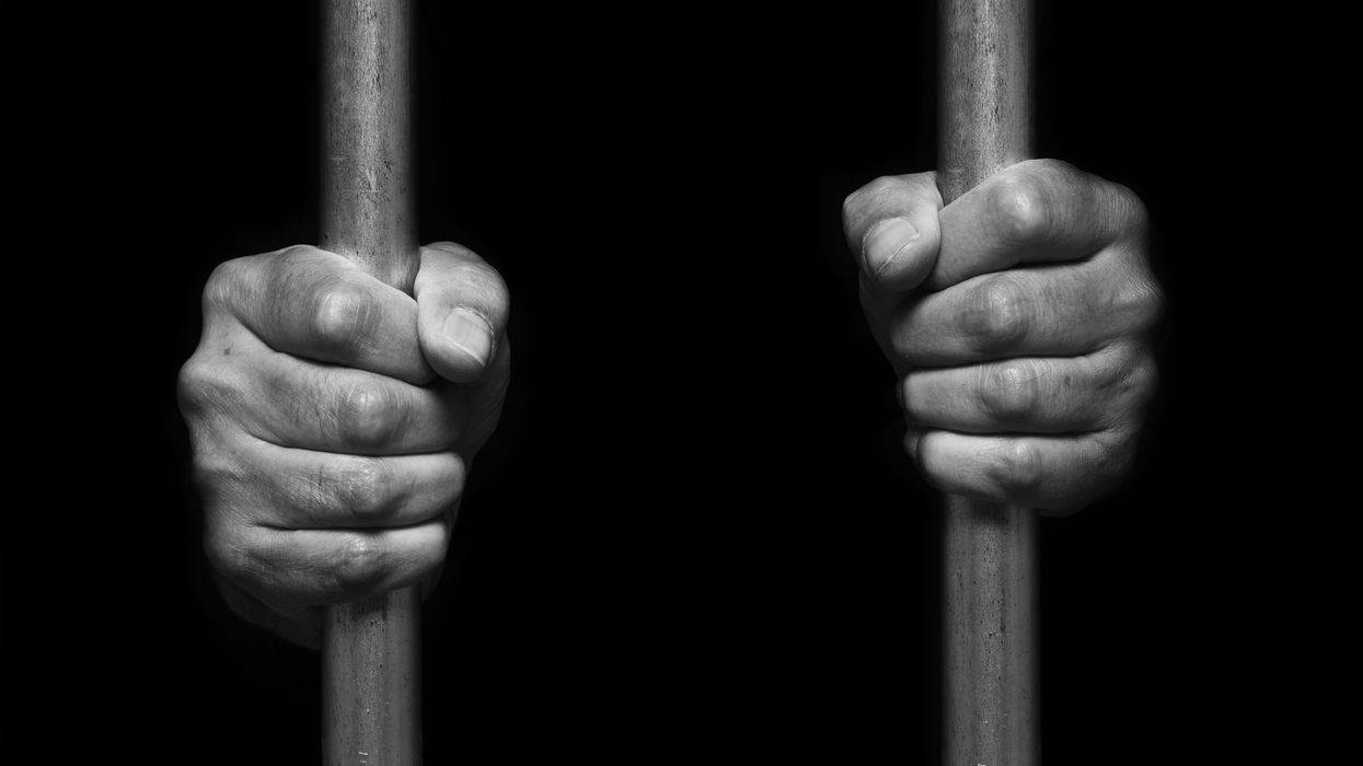 Person's hands holding prison bars