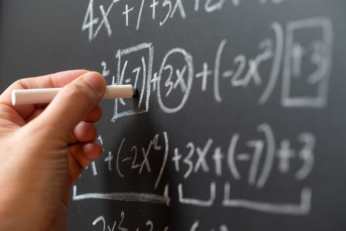Person writing math equations on a chalkboard.