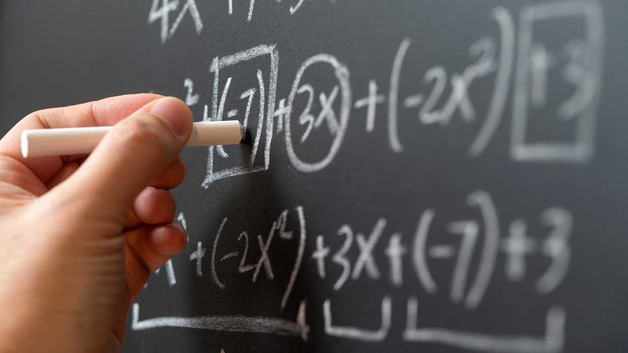 Person writing math equations on a chalkboard.