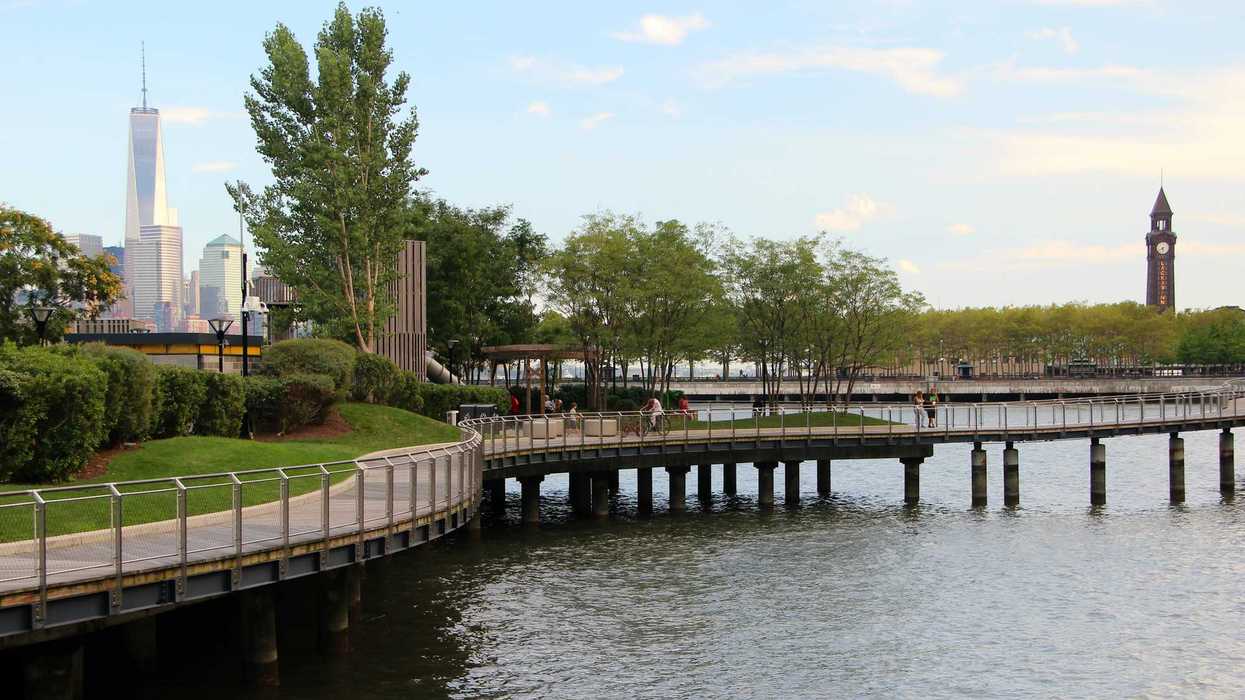 Pier C Park waterfront walkway and in the background the One World Trade Center on the left and the Erie-Lackawanna Railroad and Ferry Terminal Clock Tower on the right