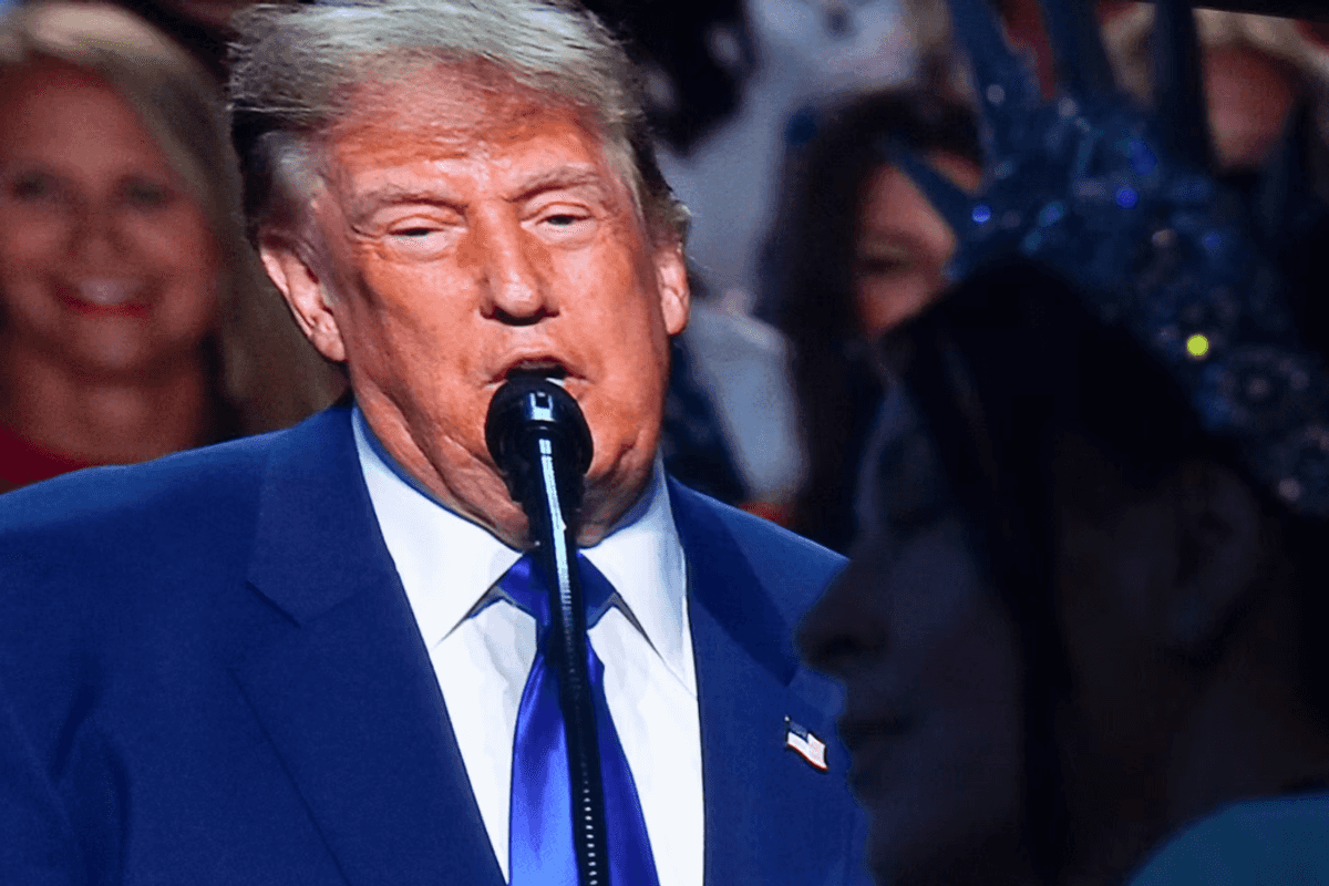 President Trump on a large TV screen behind a woman wearing a statue of liberty inspired crown.