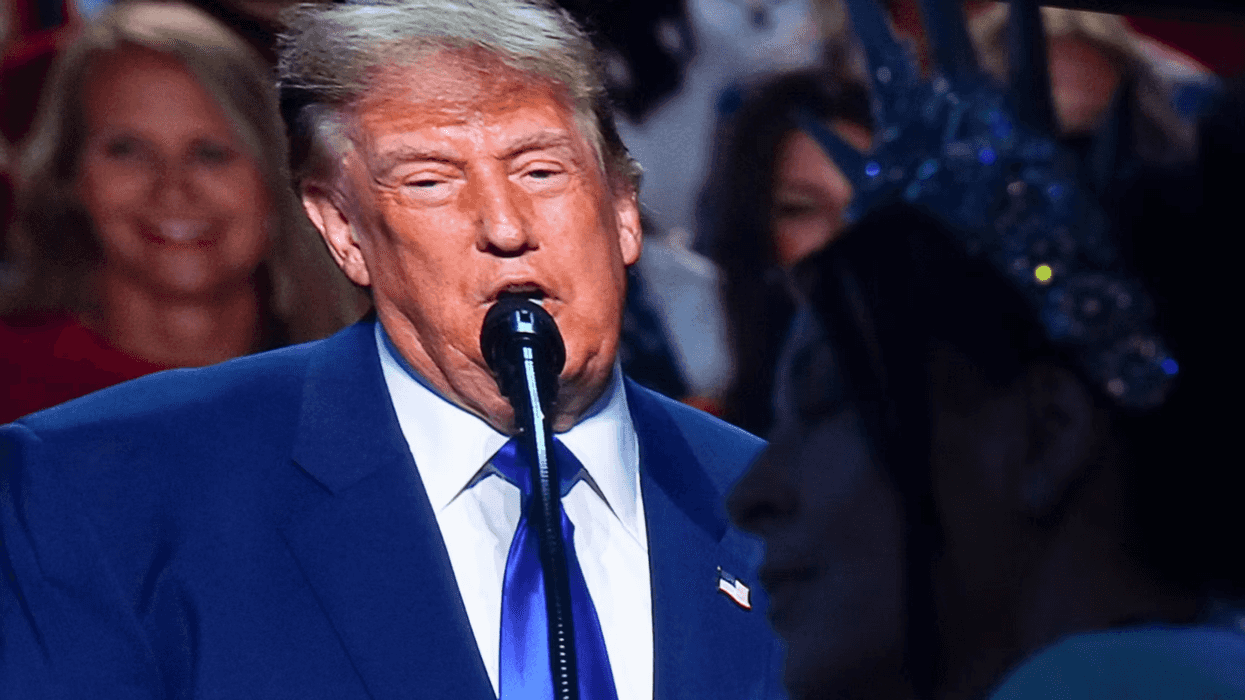 President Trump on a large TV screen behind a woman wearing a statue of liberty inspired crown.