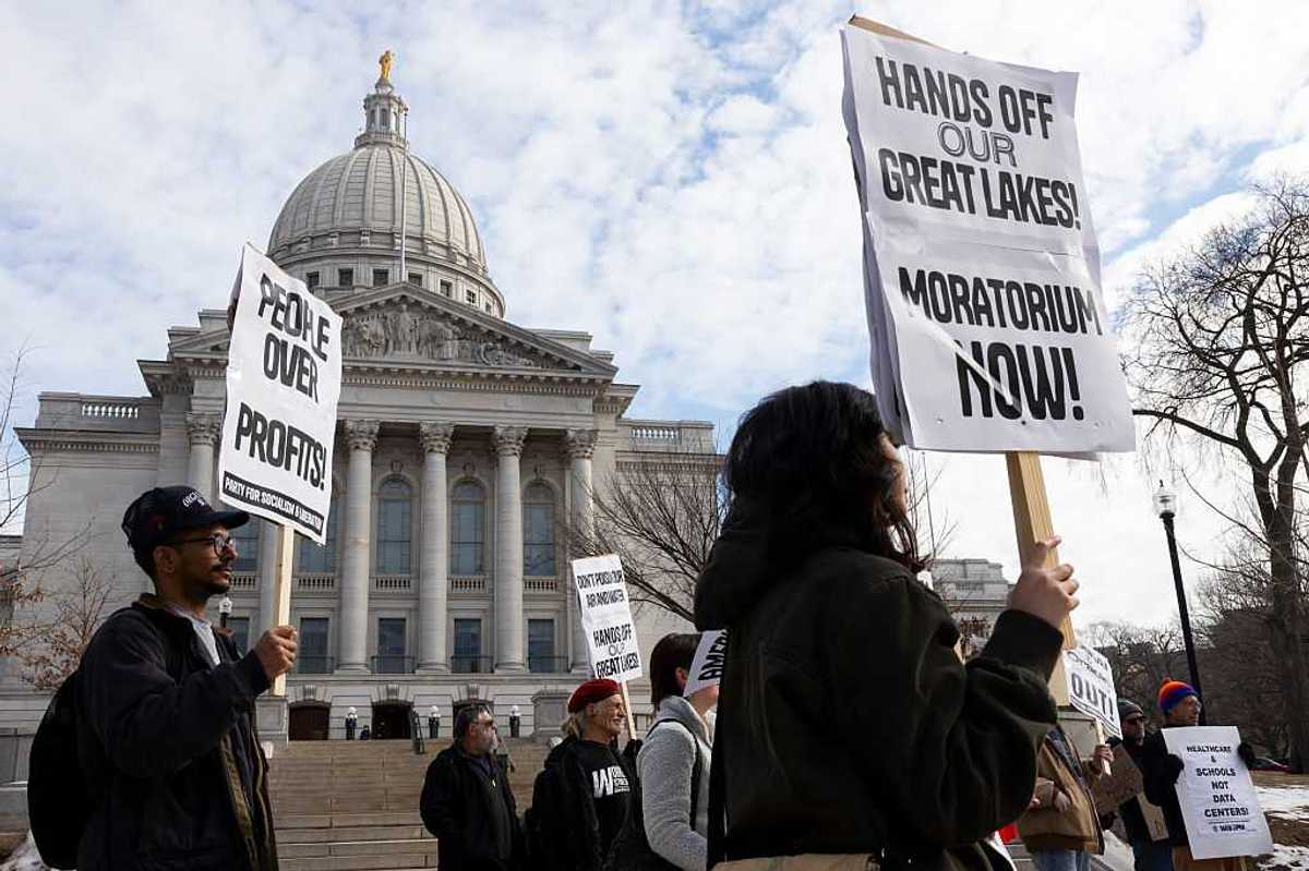 Protesters gather at the Wisconsin State Capitol, holding signs.