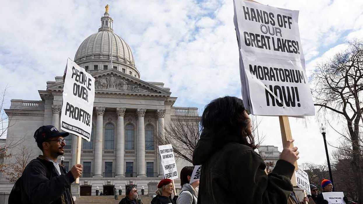 Protesters gather at the Wisconsin State Capitol, holding signs.