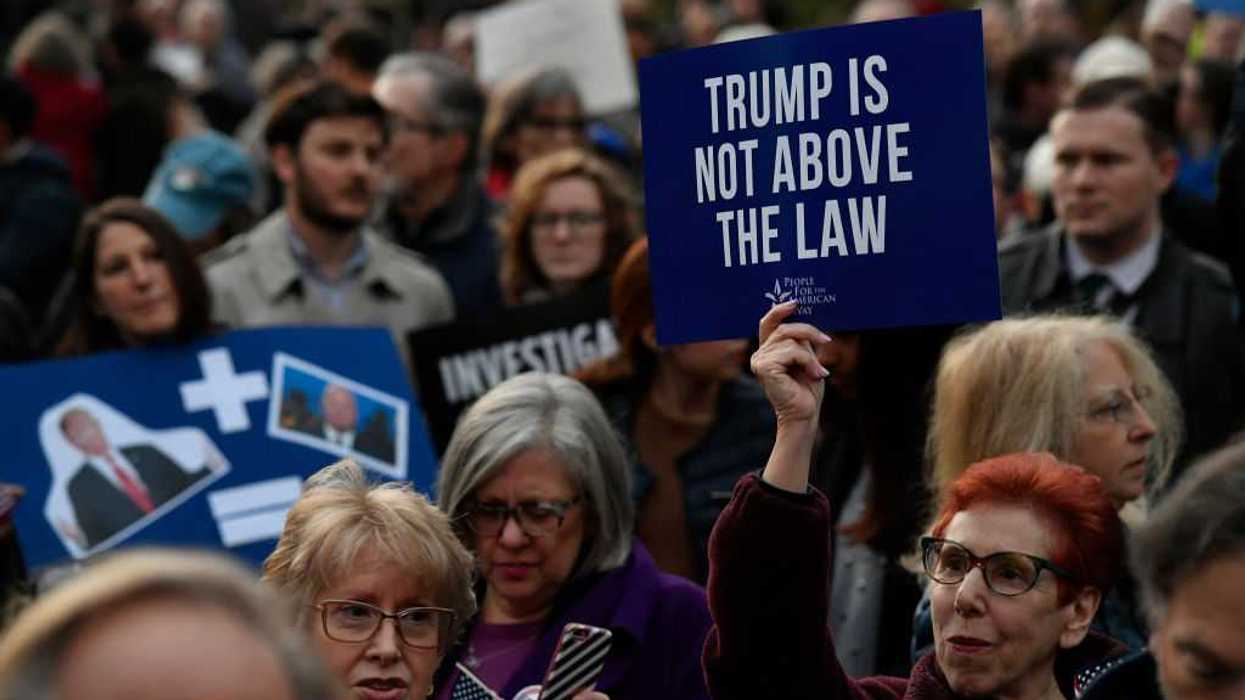 Protestors holding signs at a rally, one reads, "Trump is not above the law."