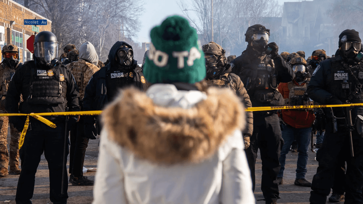 Protestors on one side of a caution tape line and people in mis-matching military gear on the other side.