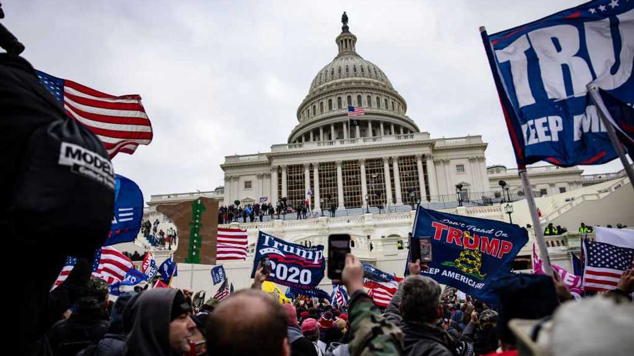 Protestors standing outside of the U.S. Capitol with flags and signs.