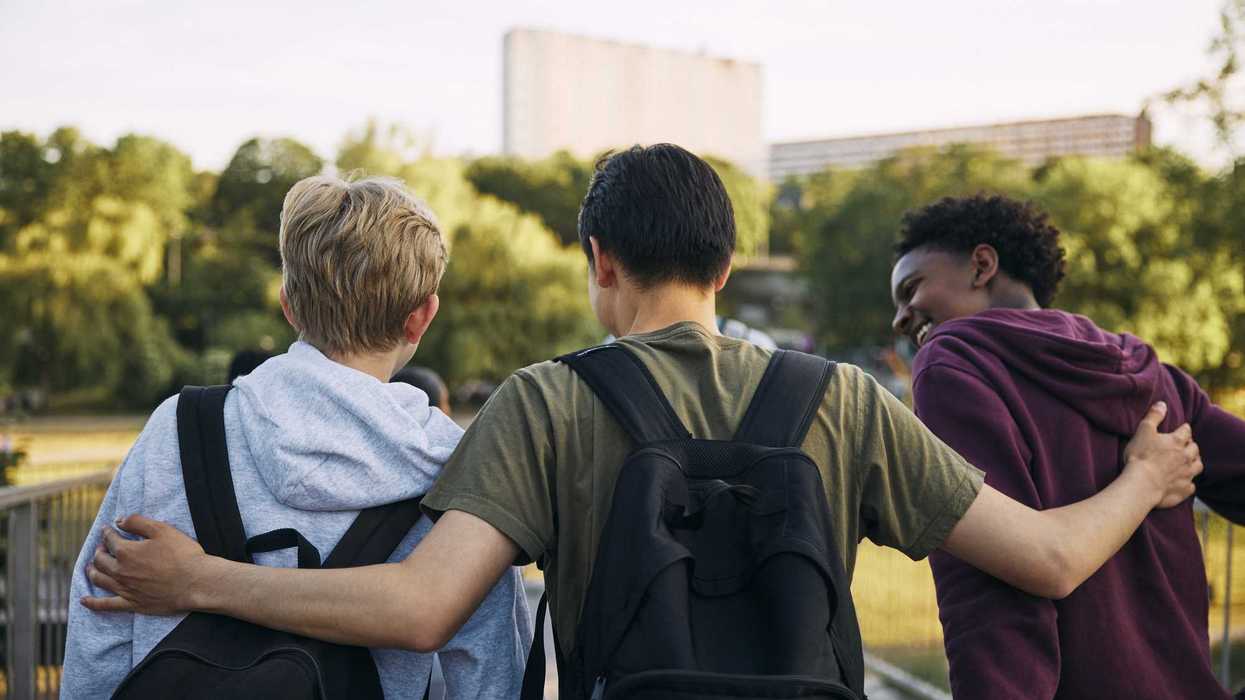 Rear view of teenage boy walking with arm around friends