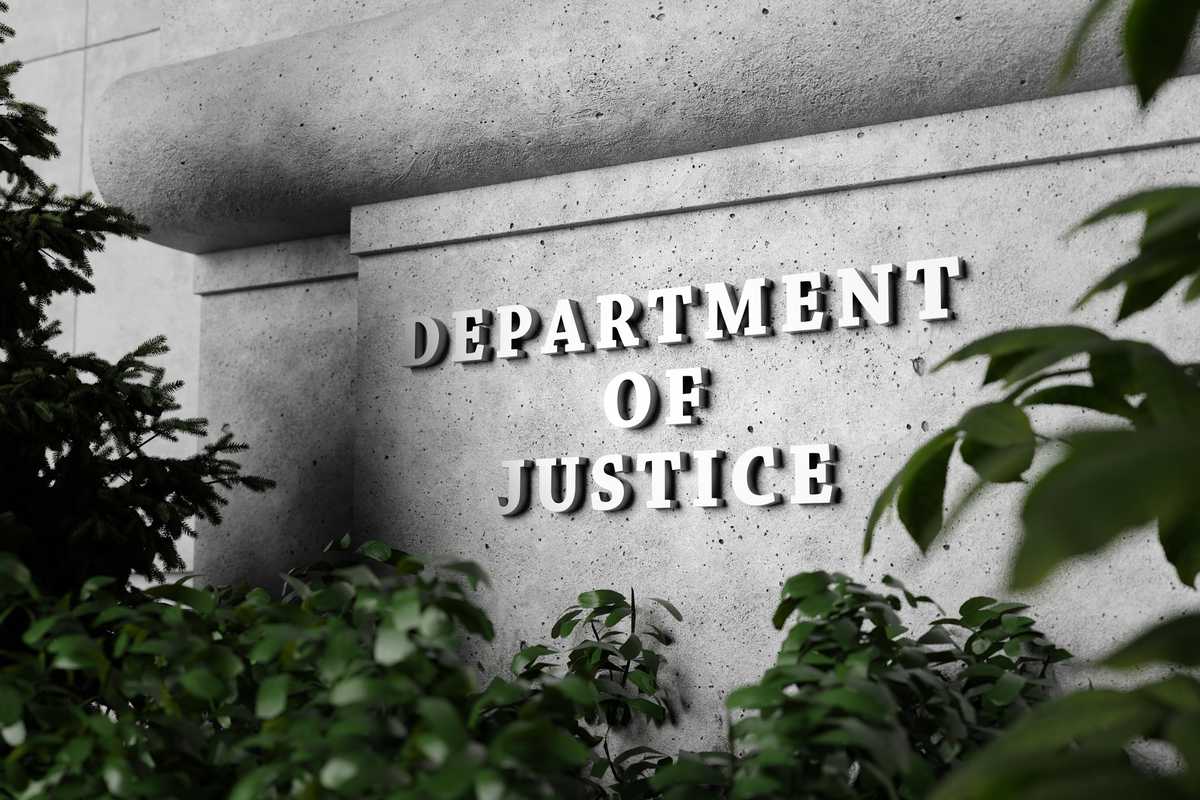 Silver sign of Department of Justice on a classical concrete wall with plants as foreground.