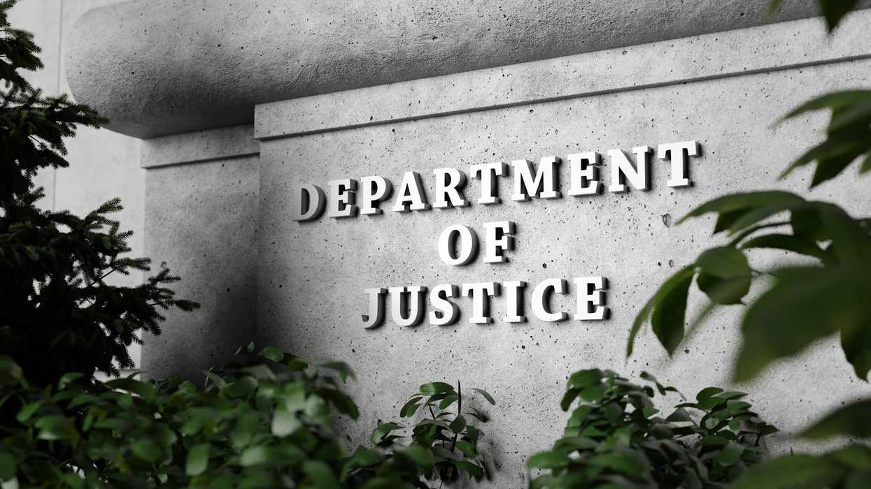 Silver sign of Department of Justice on a classical concrete wall with plants as foreground.