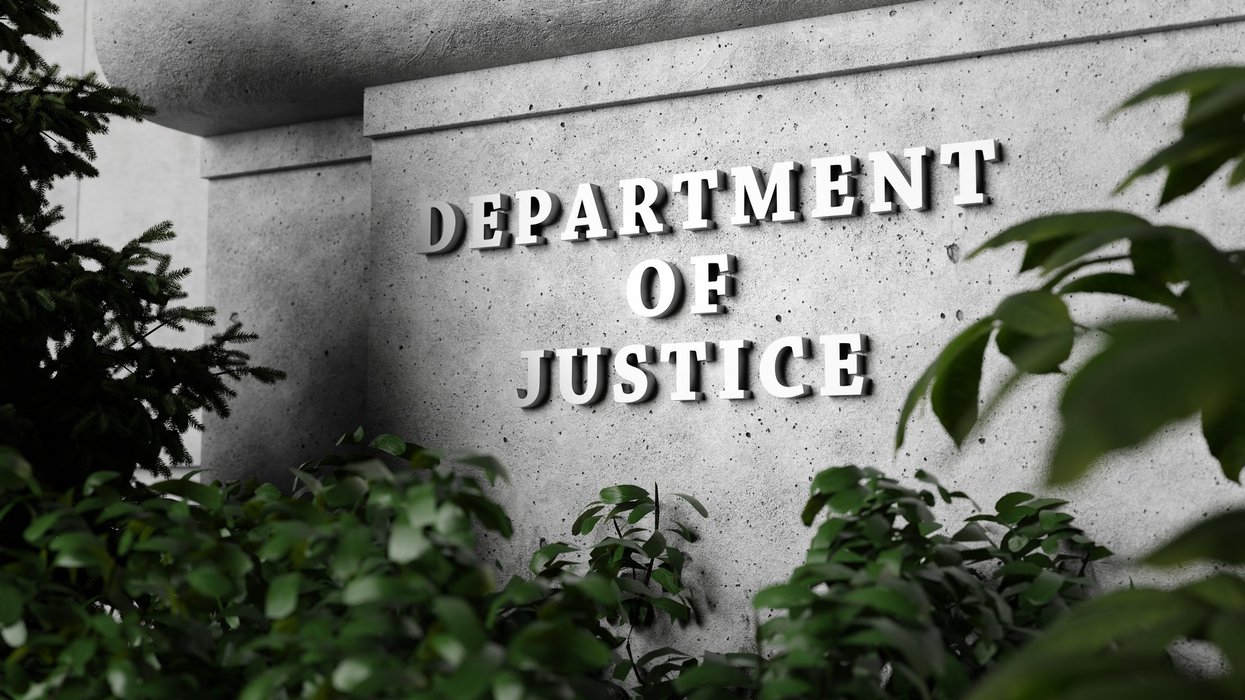 Silver sign of Department of Justice on a classical concrete wall with plants as foreground.