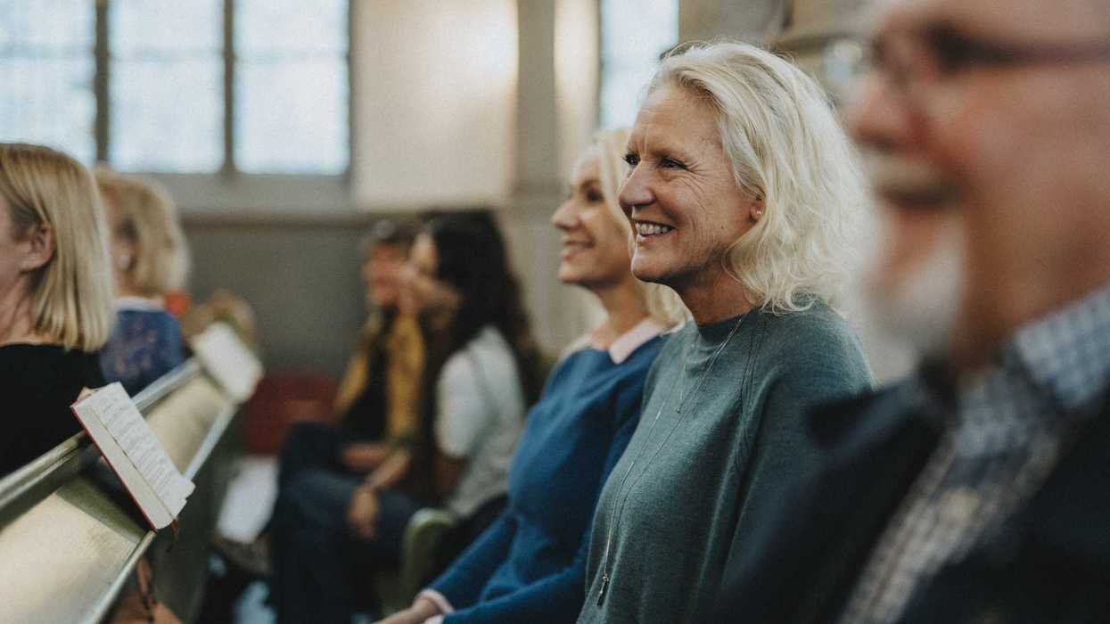 Smiling mature woman sitting next to other people, all sitting at church