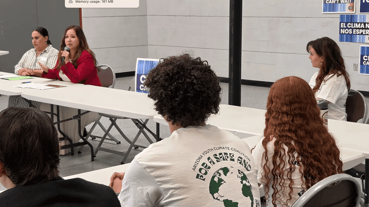 Students sitting at a table listening to a speaker.